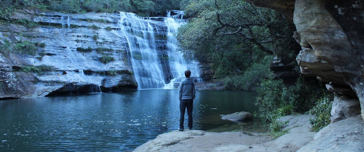 A waterfall cascading into a river surrounded by rocky terrain and dense foliage.
