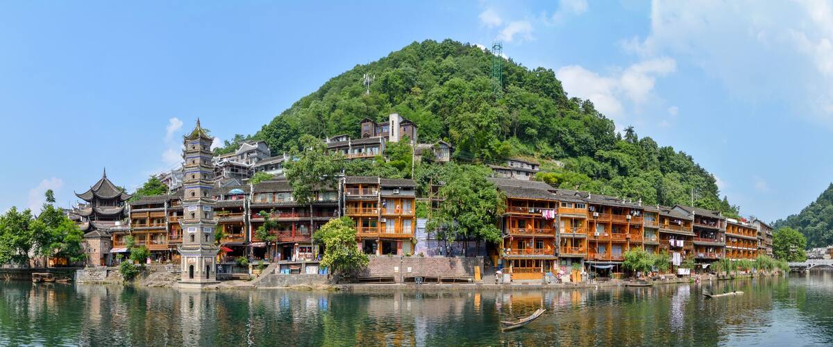 A traditional Chinese building complex by a lake with a mountain backdrop.