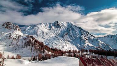 A snow-covered mountain range with a clear sky and scattered clouds.