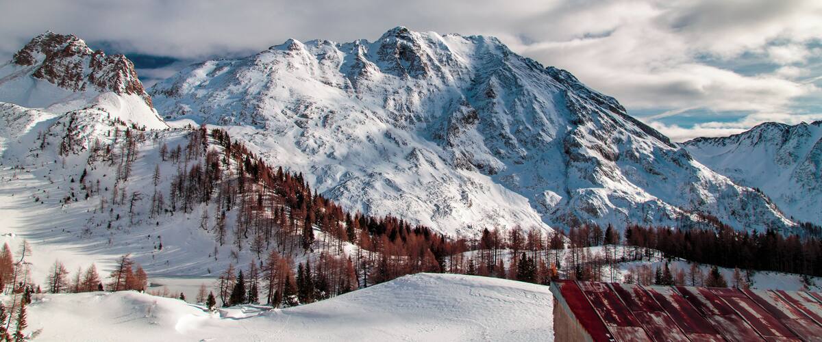 A snow-covered mountain range with a clear sky and scattered clouds.