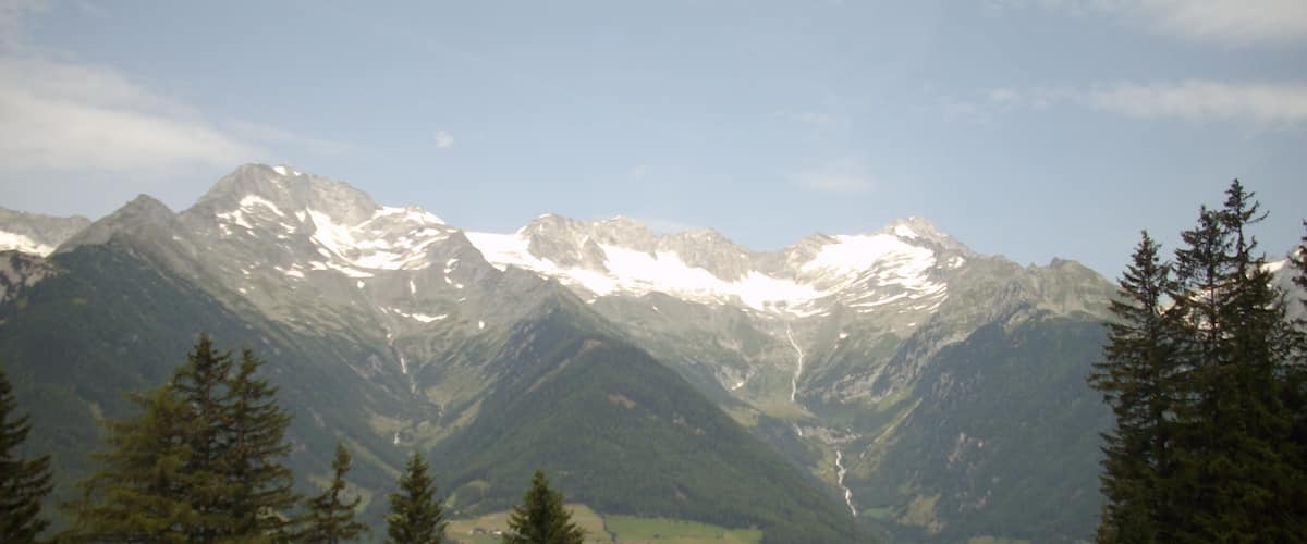 A mountain range with snow-capped peaks, a valley with greenery, and a clear sky.