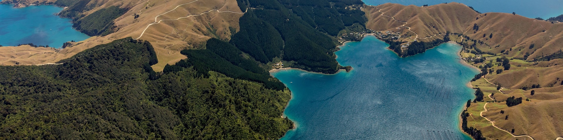 A coastal landscape with rugged hills, a winding road, and a large body of water.