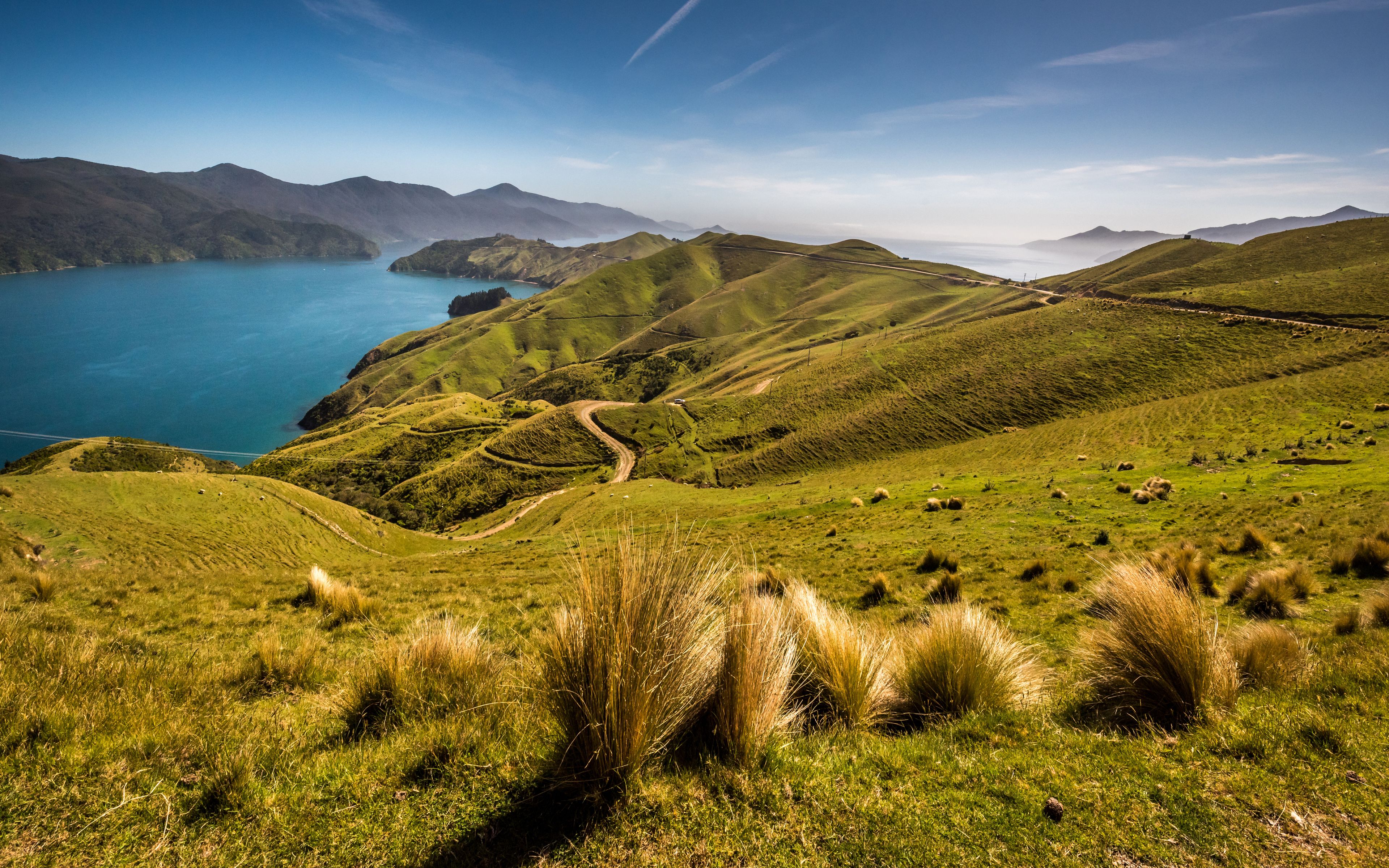 A coastal landscape with rolling hills, a winding road, and a body of water.