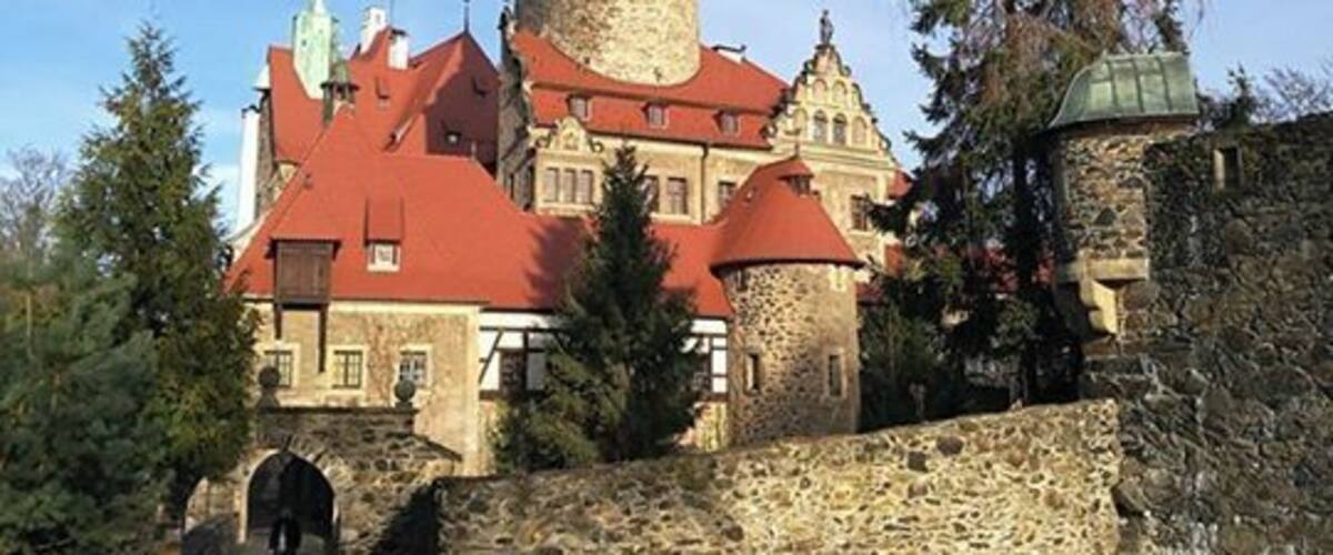 A historic building with a red roof, a prominent tower, and a stone wall.