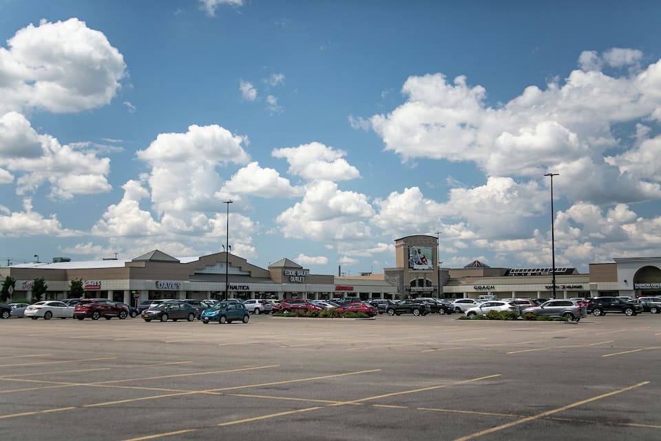 Un estacionamiento con varios coches y un centro comercial al fondo.
