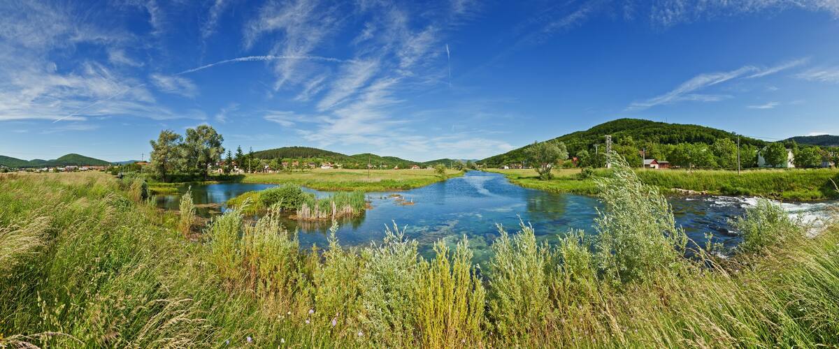 A clear river with surrounding greenery and hills.