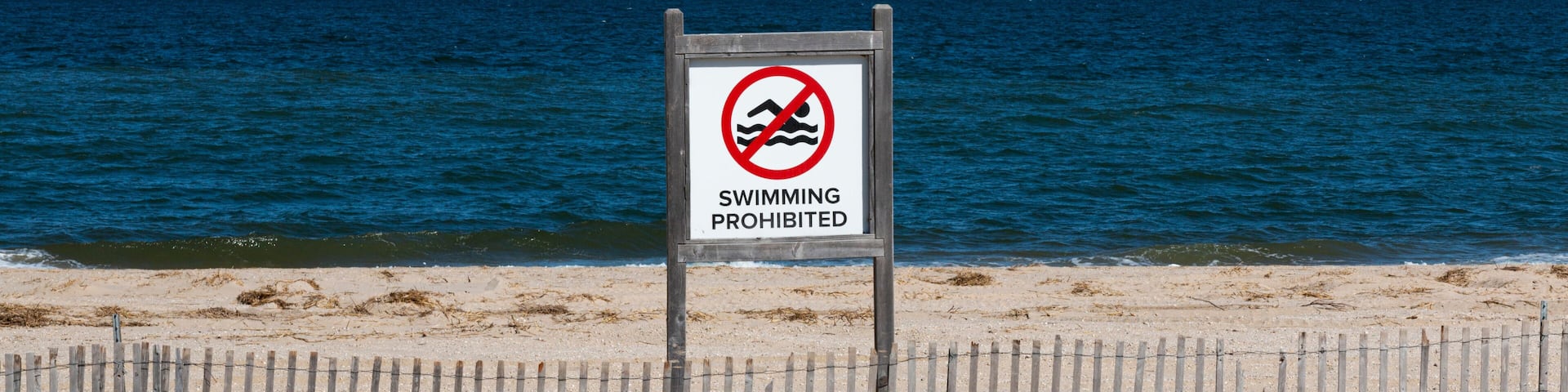 A beach with a sign prohibiting swimming.