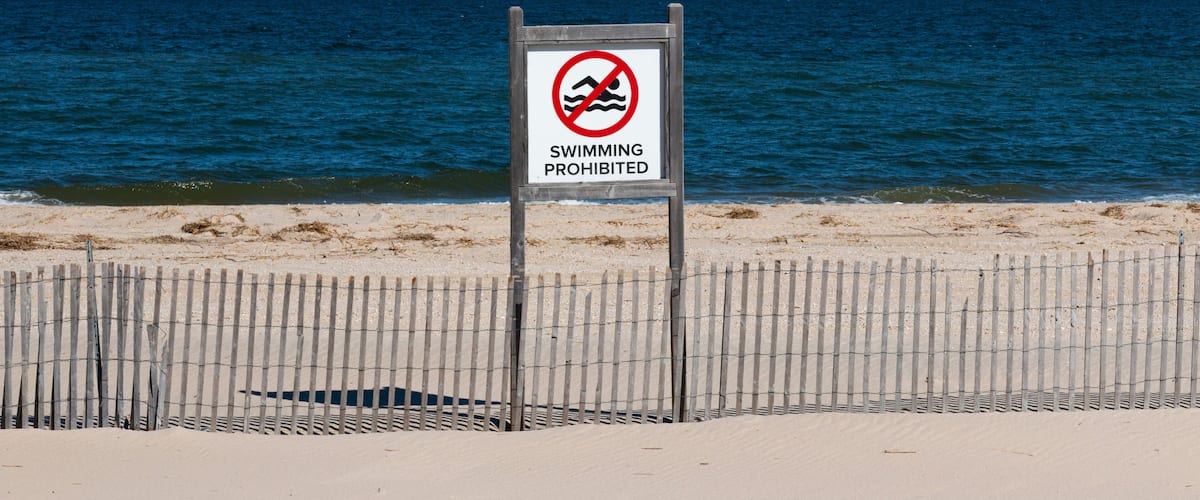 A beach with a sign prohibiting swimming.