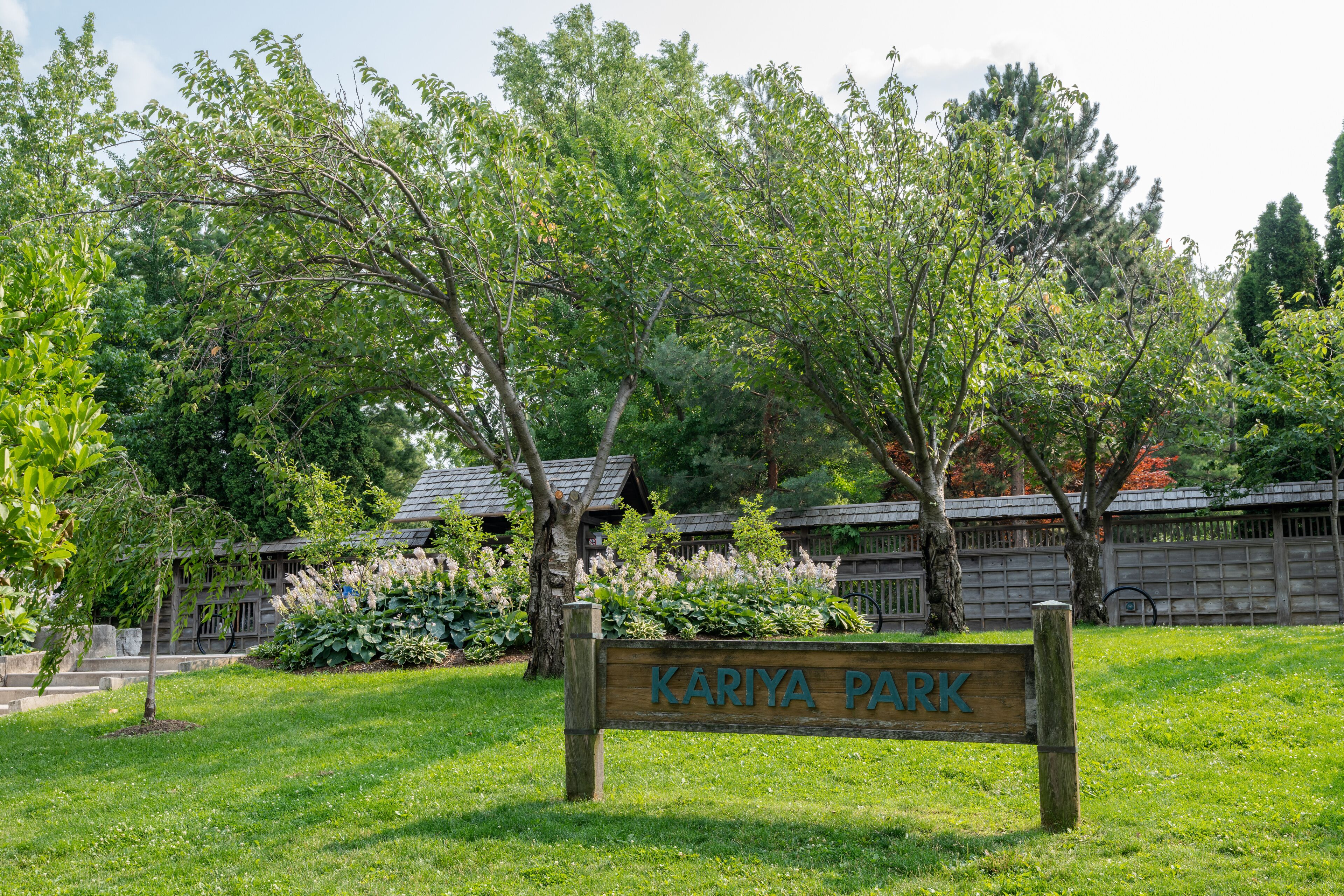 A wooden sign that reads "KARIYA PARK" surrounded by lush green trees and grass.