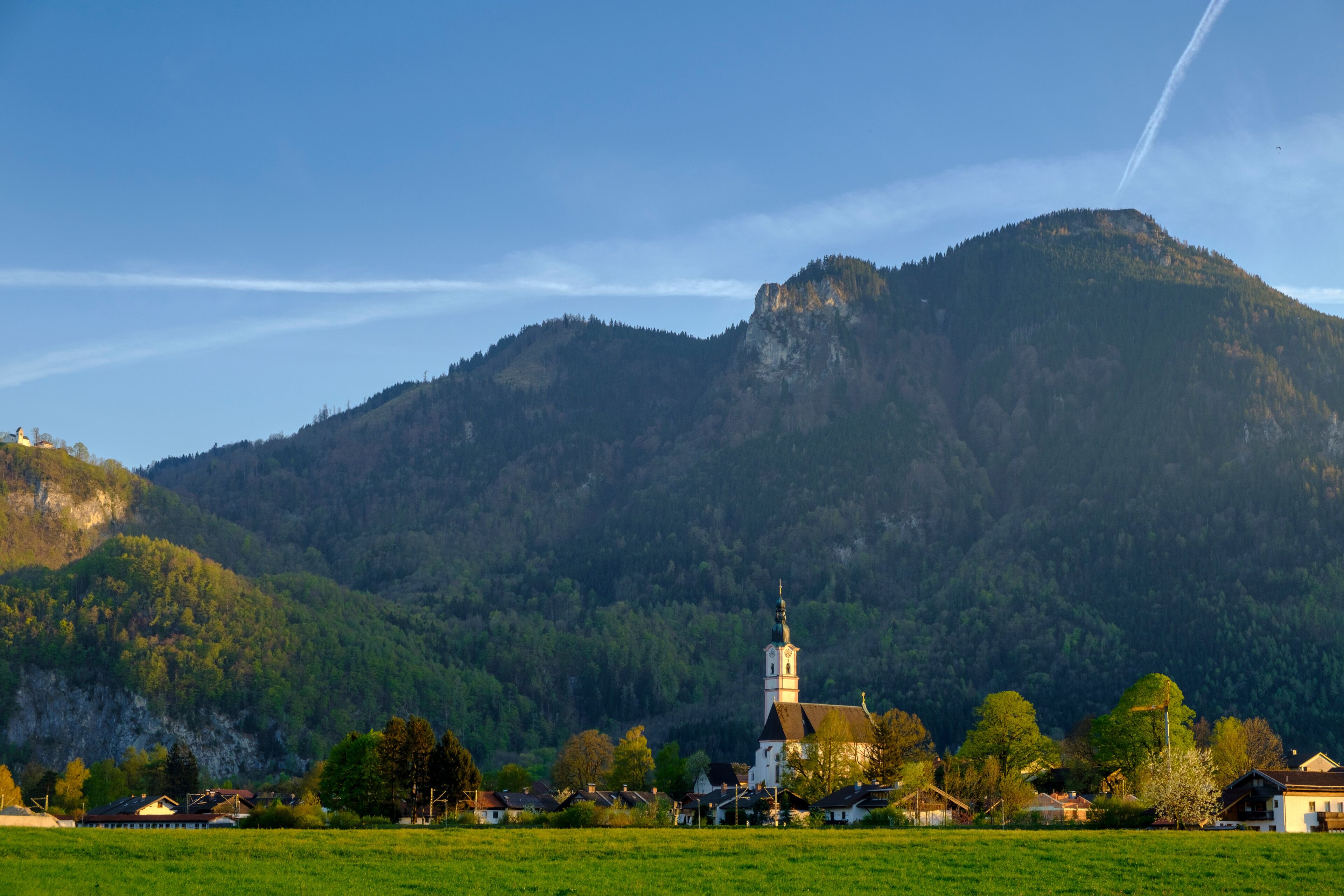 A church with a tall steeple surrounded by a village and a mountain in the background.