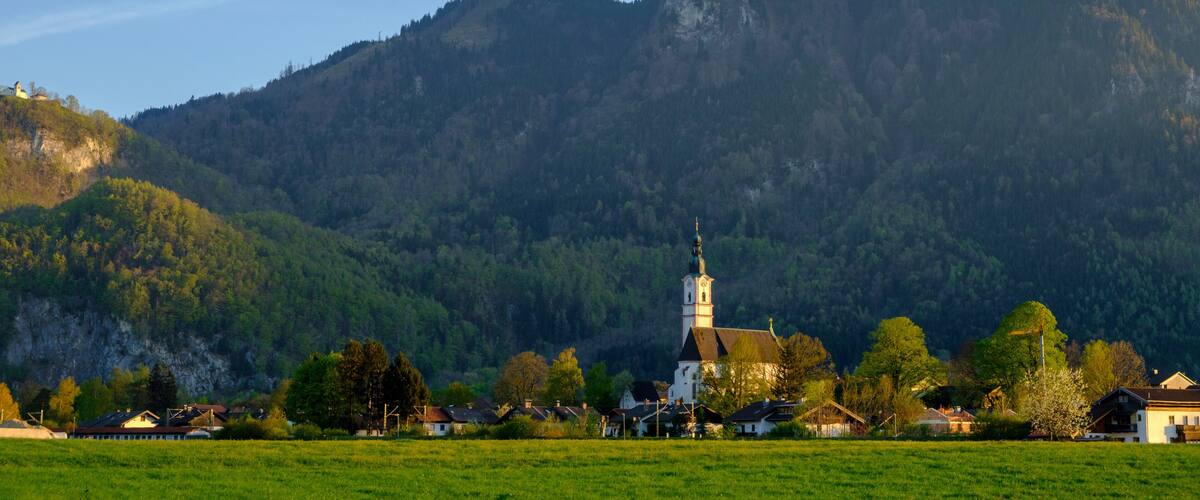 A church with a tall steeple surrounded by a village and a mountain in the background.