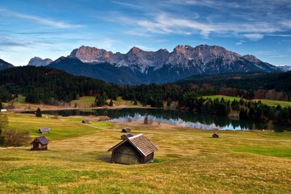 A rural landscape with a lake, mountains, and wooden houses.