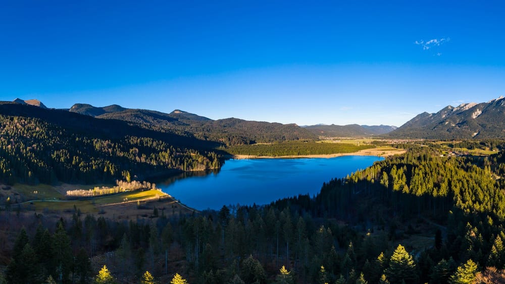 Eine Berglandschaft mit einem See, umgeben von dichten Wäldern und fernen Gipfeln.