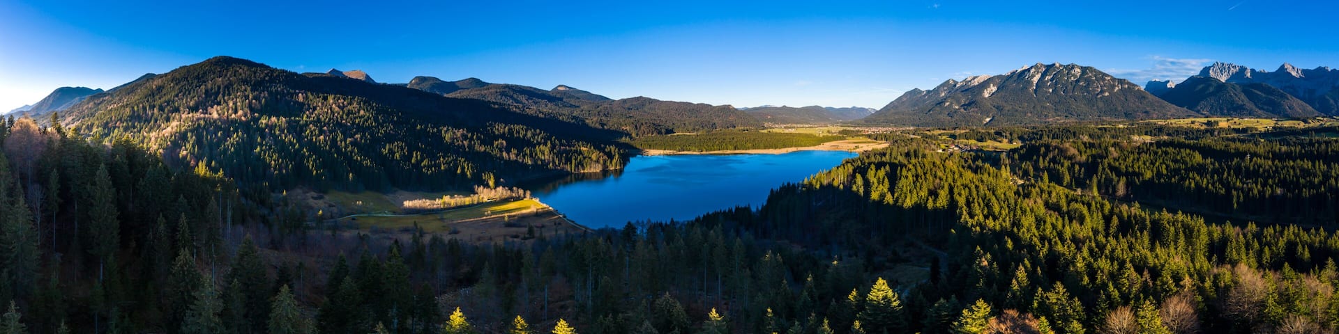 A mountainous landscape with a lake surrounded by dense forests and distant peaks.