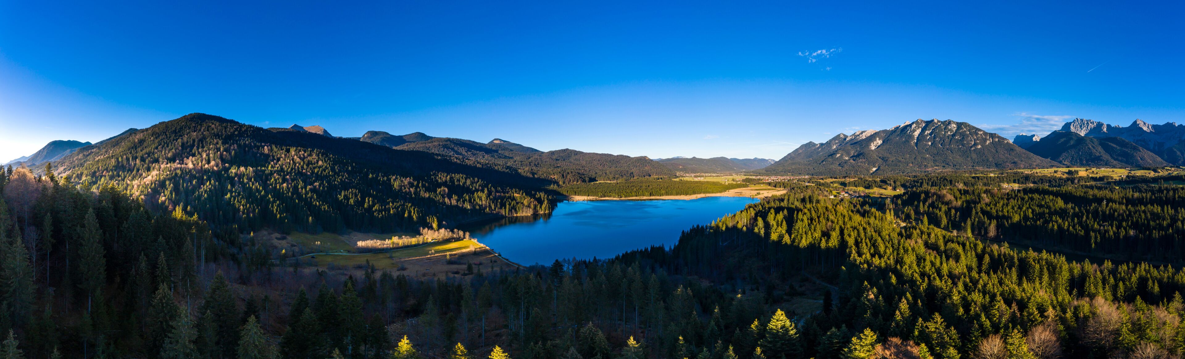 A mountainous landscape with a lake surrounded by dense forests and distant peaks.