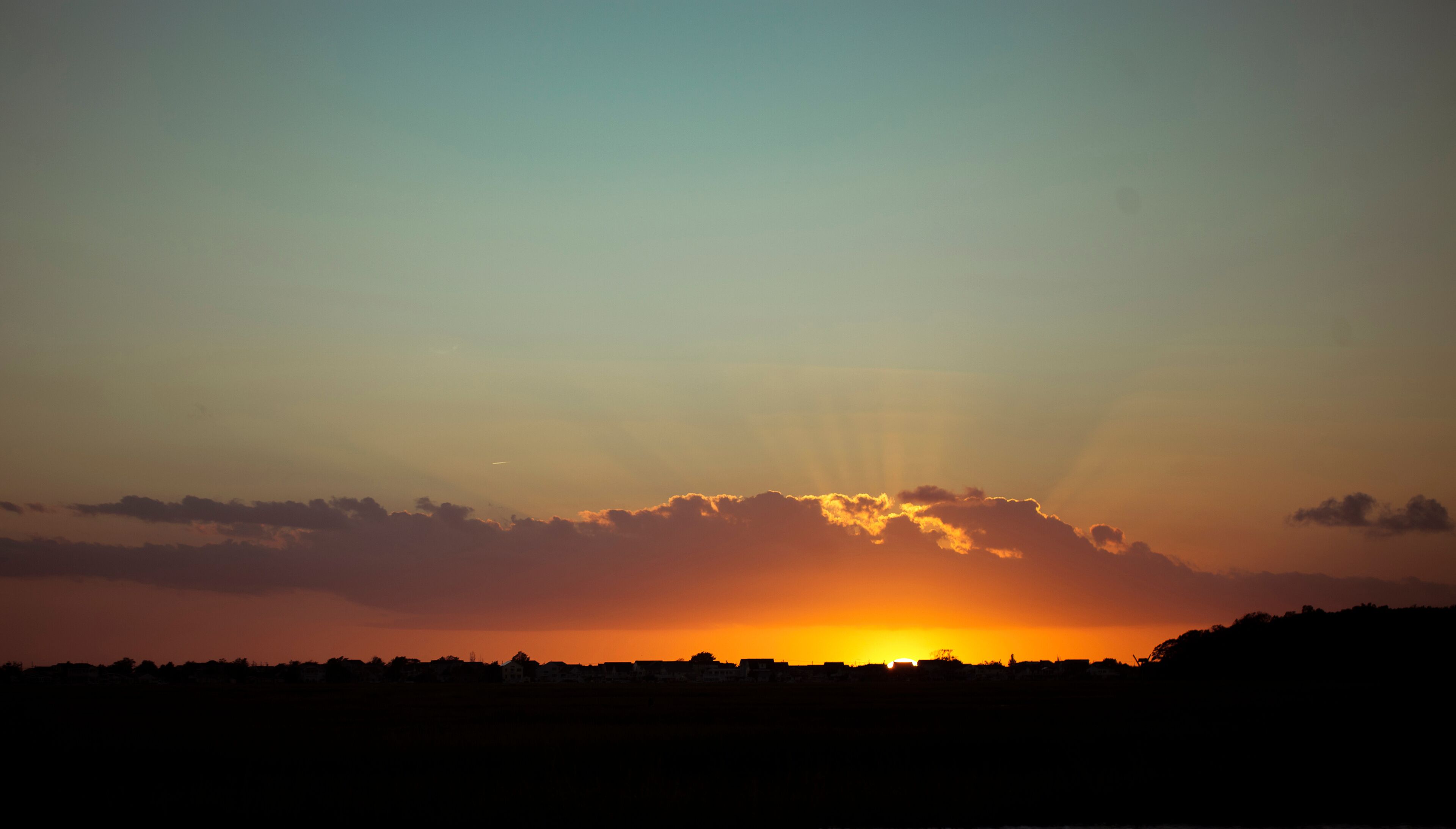 A sunset over a silhouette of a town with a clear sky.