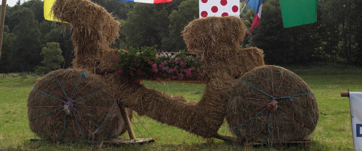 Two hay bale sculptures in a field with a backdrop of flags and flowers.