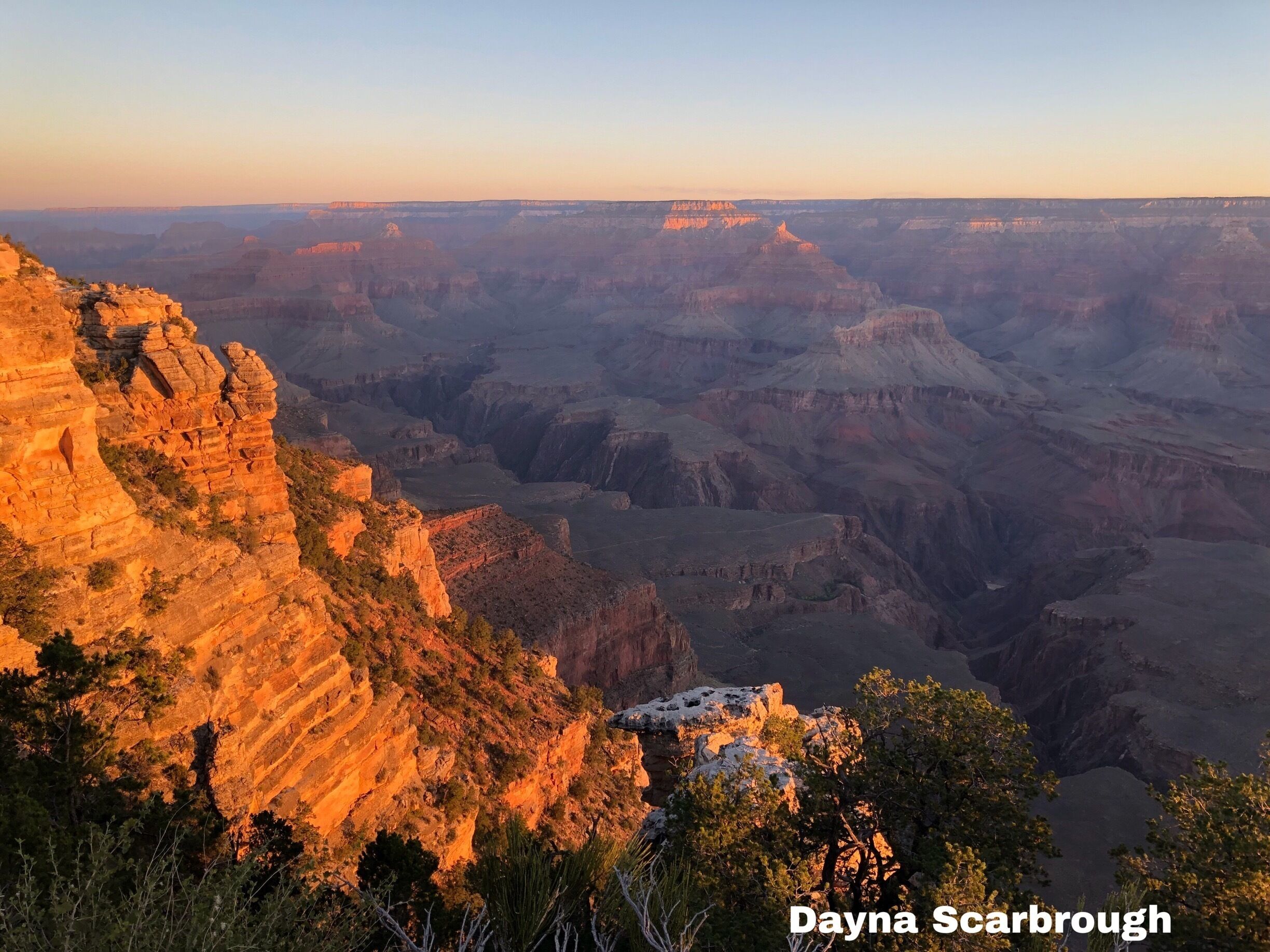 A canyon landscape with layered rock formations and a small building in the foreground.