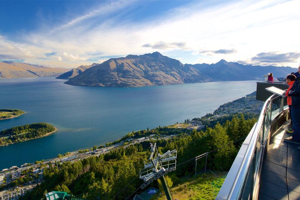 Een panoramisch uitzicht op een meer, omringd door bergen, een skilift en een stad eronder.