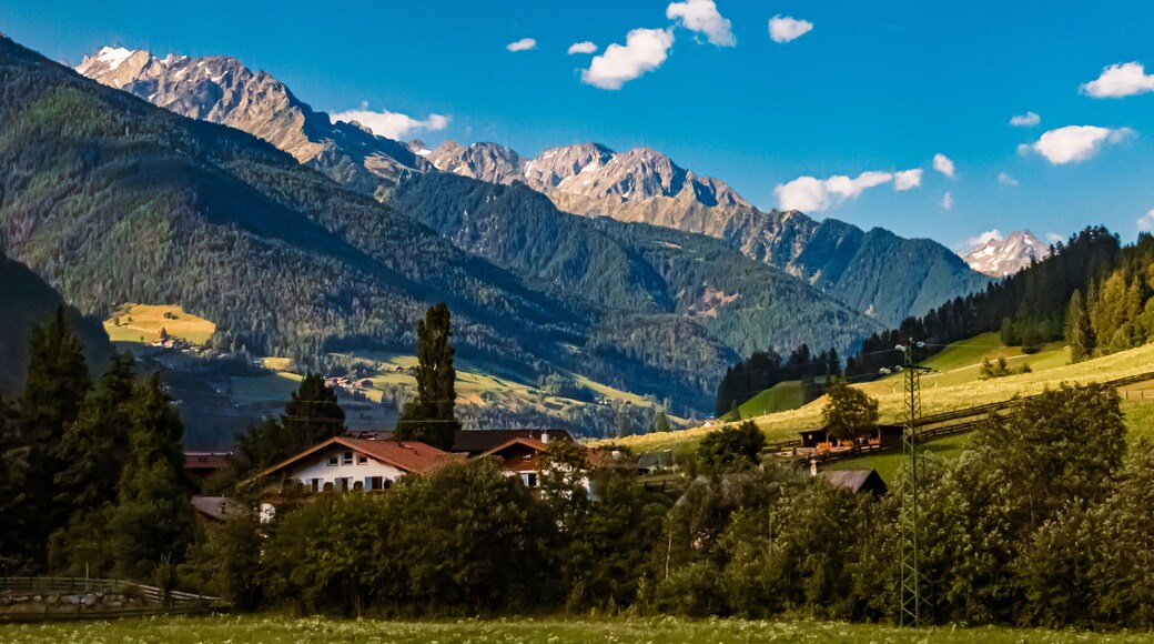 Eine Berglandschaft mit einem Haus im Vordergrund und schneebedeckten Gipfeln im Hintergrund.