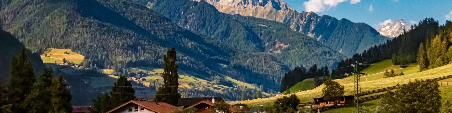 Un paisaje montañoso con una casa en primer plano y picos nevados al fondo.