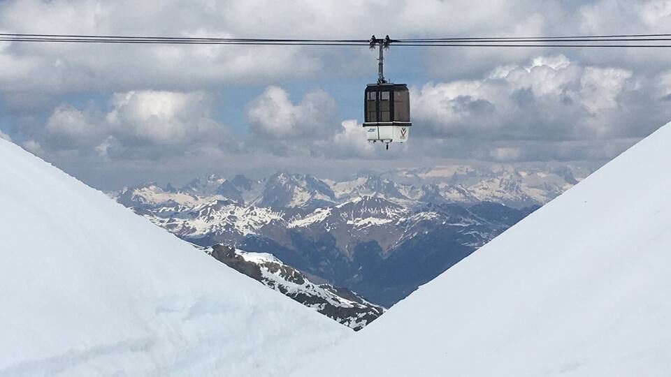 Un teleférico suspendido sobre un paisaje montañoso nevado con cielo despejado.