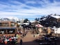 A snowy mountain town with wooden buildings, outdoor seating, and a clear sky.