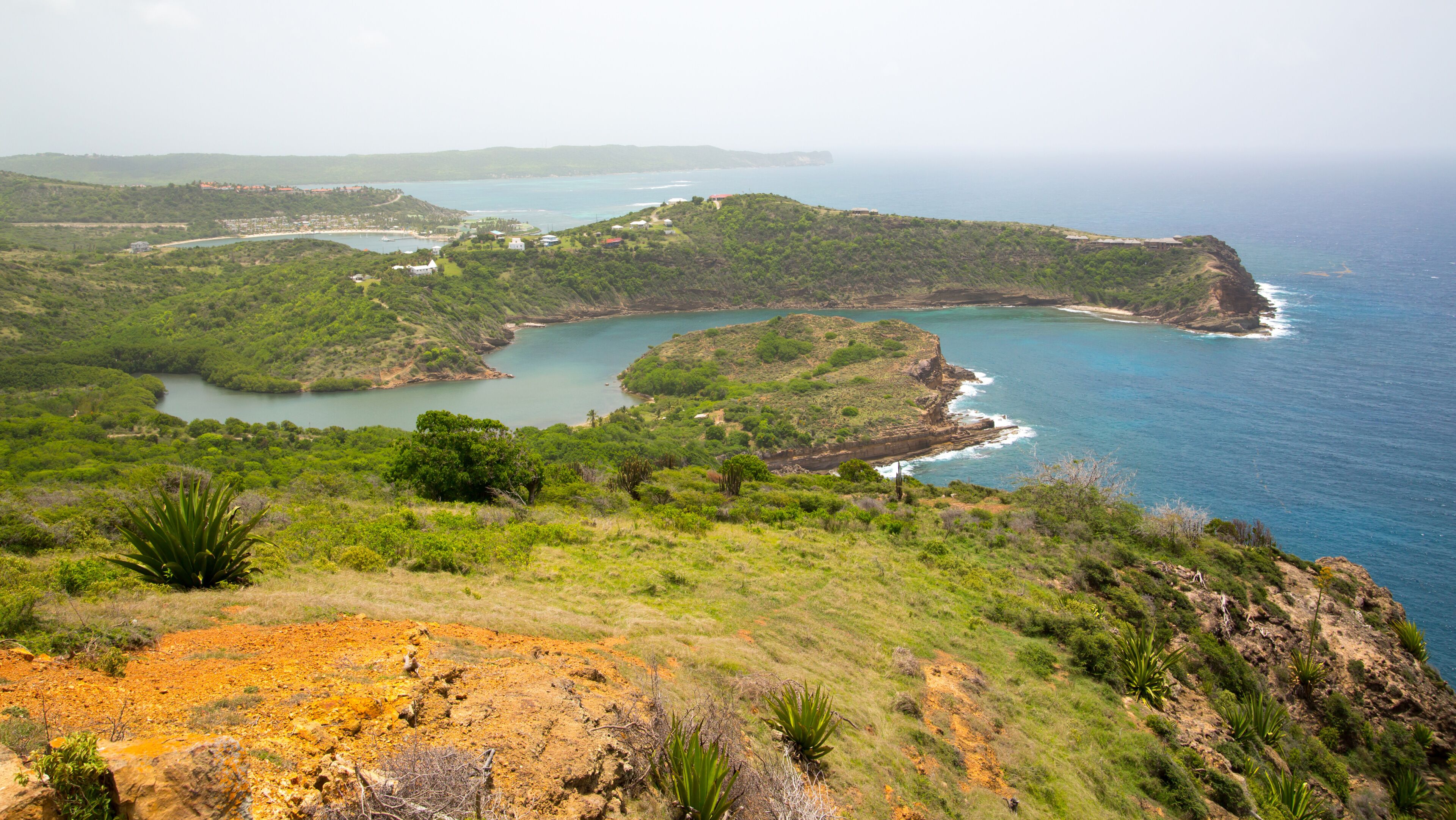 Un paisaje costero con una bahía, colinas verdes y un acantilado que domina el mar.