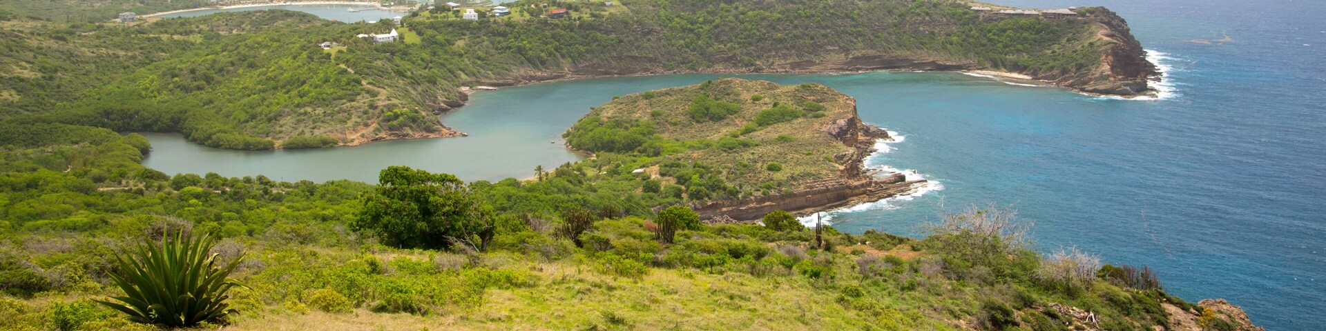 Un paisaje costero con una bahía, colinas verdes y un acantilado que domina el mar.