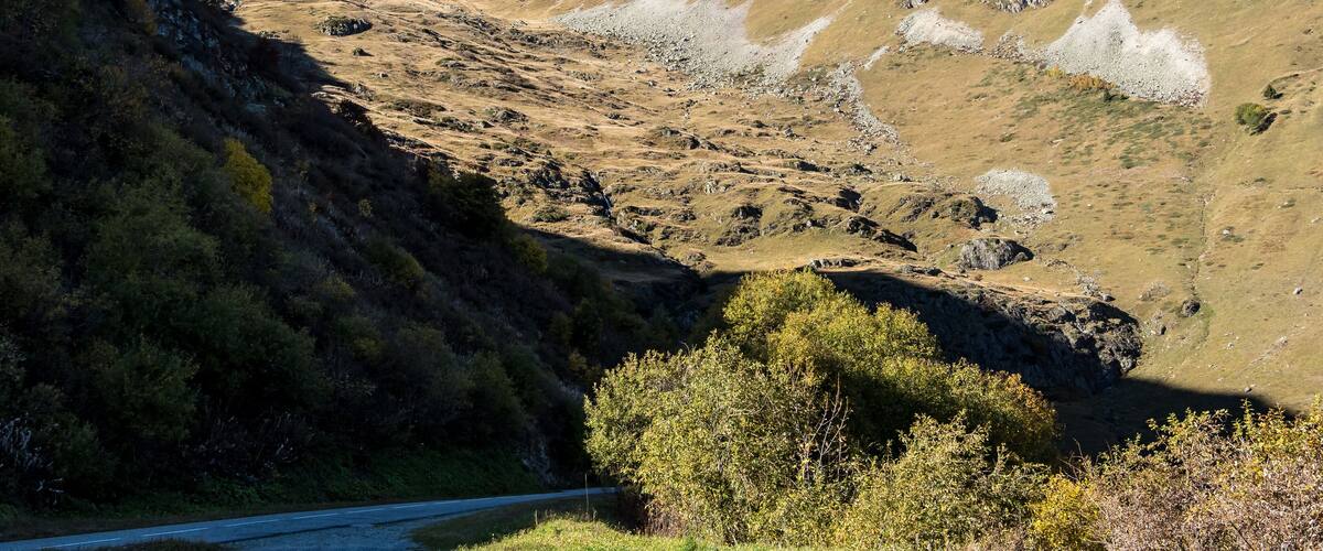 A mountainous landscape with a winding road, rocky terrain, and sparse vegetation.