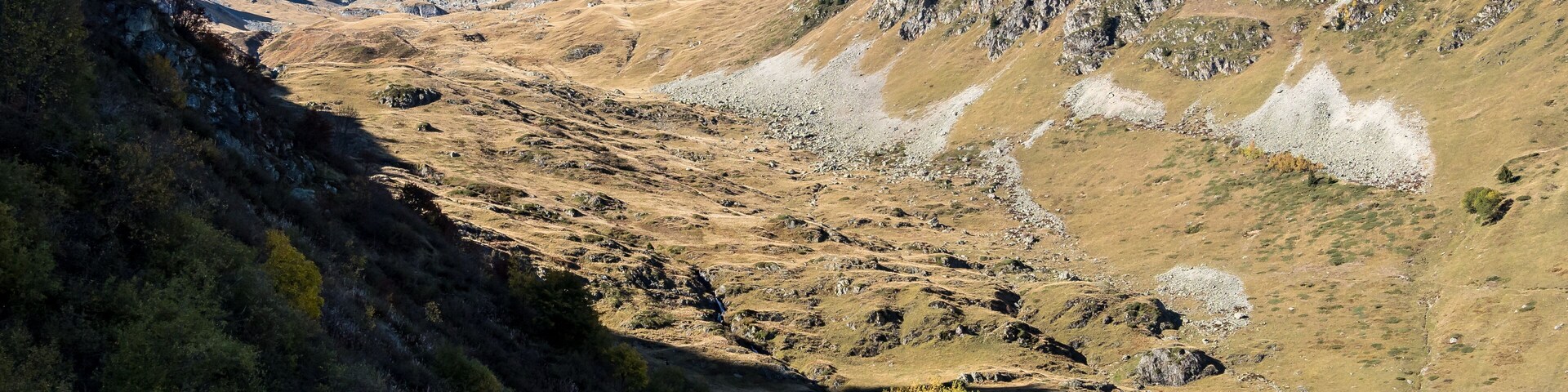 A mountainous landscape with a winding road, rocky terrain, and sparse vegetation.