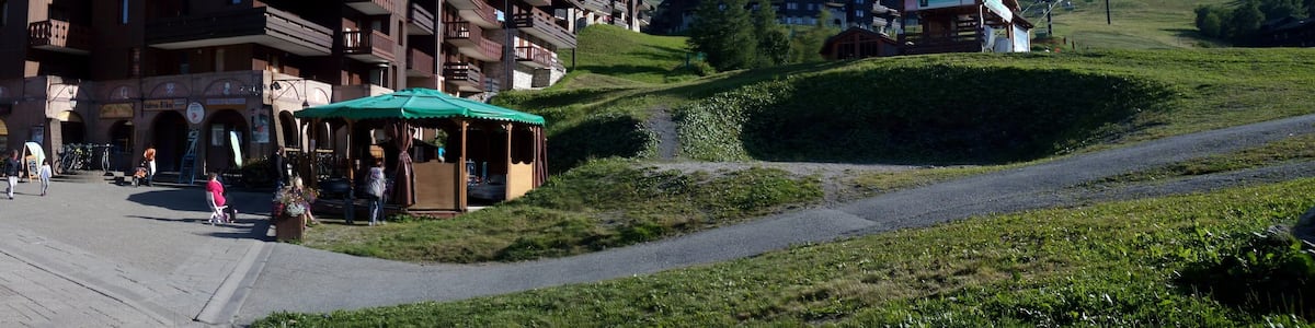 A ski resort with wooden buildings, a green-roofed gazebo, and a mountain backdrop.