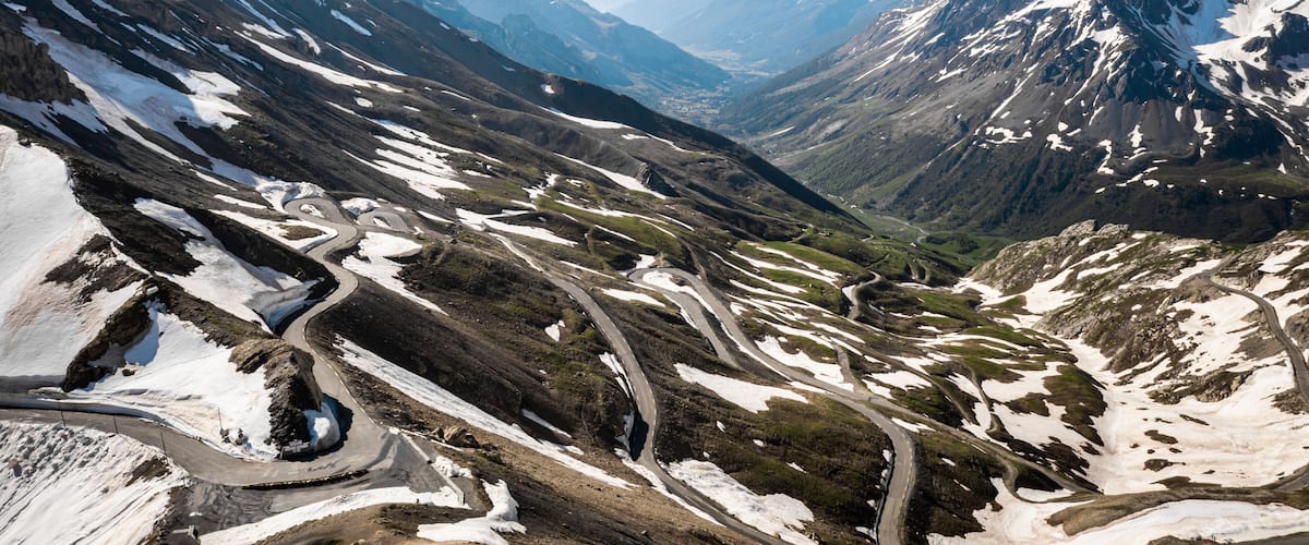 A mountain landscape with winding roads and snow patches.