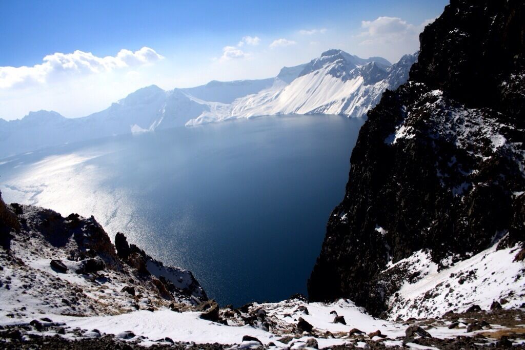 A snow-covered mountain landscape with a clear blue lake and distant mountains.