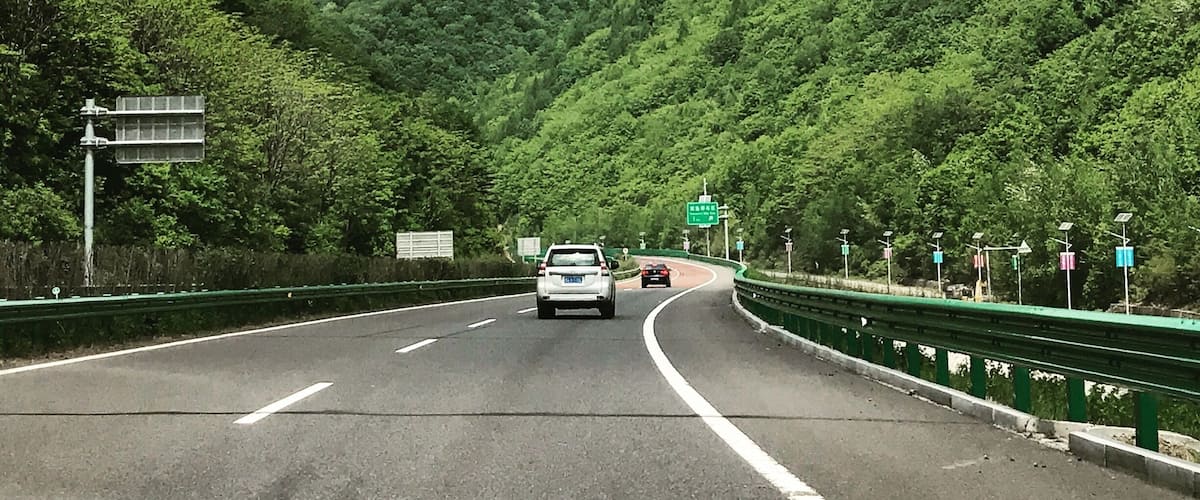 A highway with green guardrails, surrounded by lush green hills.