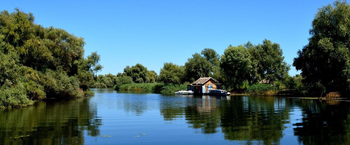 A calm river with a small houseboat on the water, surrounded by dense trees.