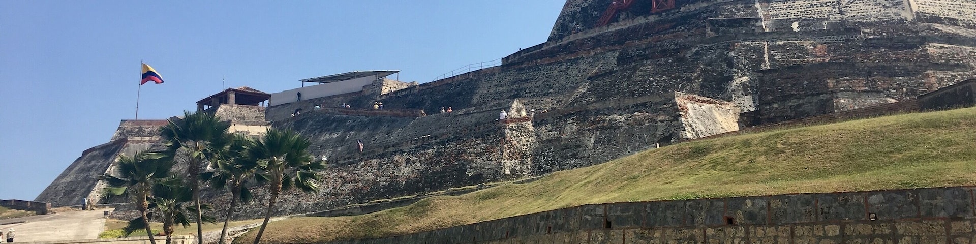 Una fortaleza histórica con una bandera, palmeras y cielo despejado.