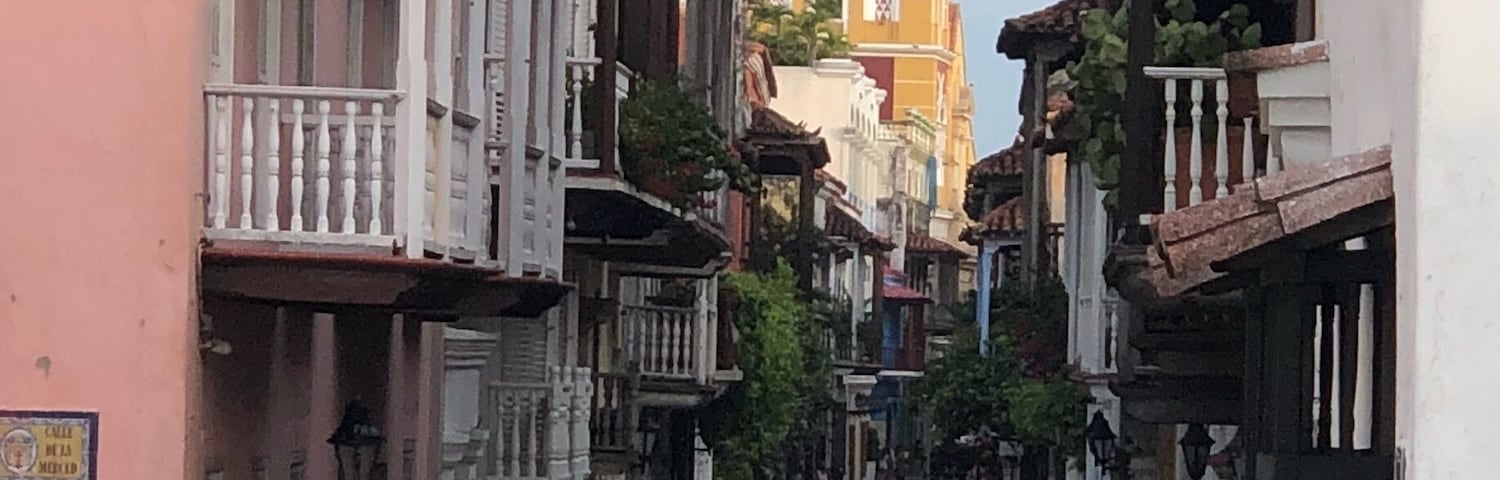 Ruas estreitas com edifícios de ambos os lados, uma charrete puxada a cavalo e uma torre de igreja imponente ao fundo.