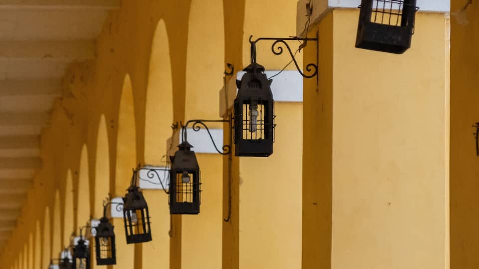 A row of yellow arches with hanging lanterns and people sitting on chairs.