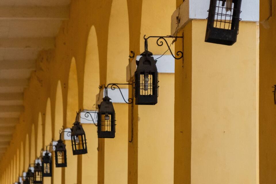 A row of yellow arches with hanging lanterns and people sitting on chairs.
