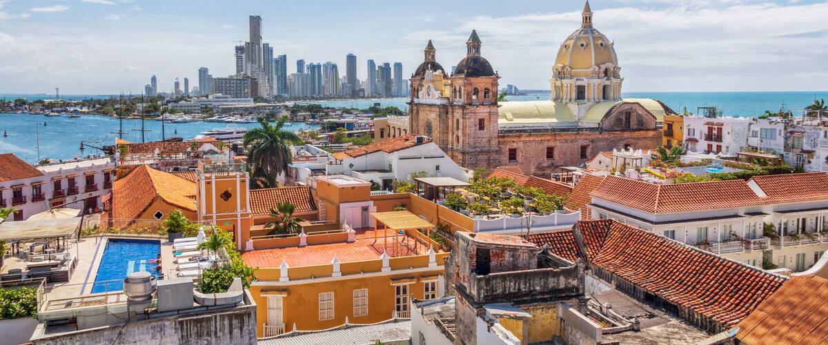 A coastal cityscape with historic buildings, a prominent church with a yellow dome, and a modern skyline in the background.