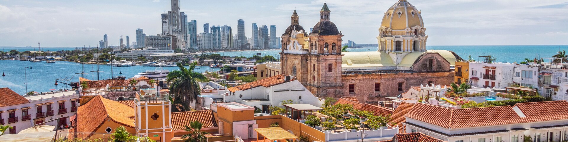 A coastal cityscape with historic buildings, a prominent church with a yellow dome, and a modern skyline in the background.