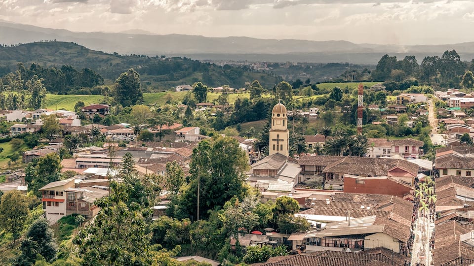 A town with a prominent church tower, surrounded by lush greenery and hilly terrain.