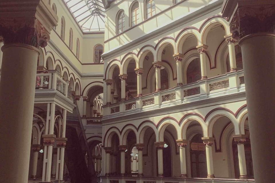 A grand atrium with a glass ceiling, arched balconies, and classical columns.