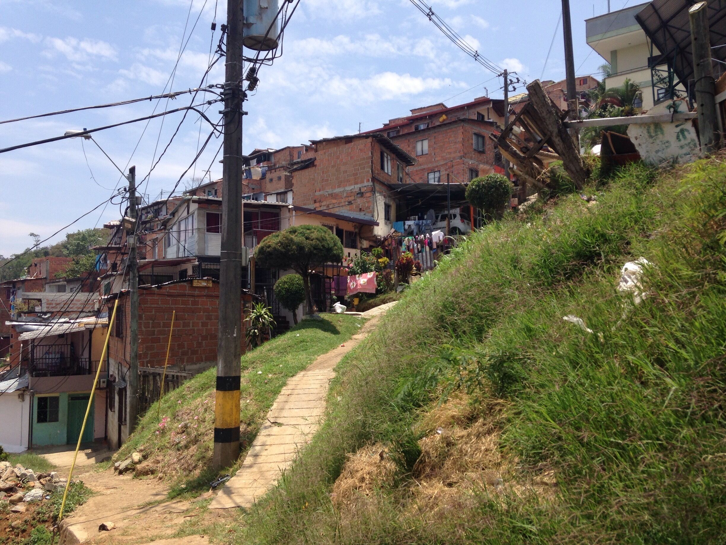 A hillside with a dirt path, buildings, and power lines.