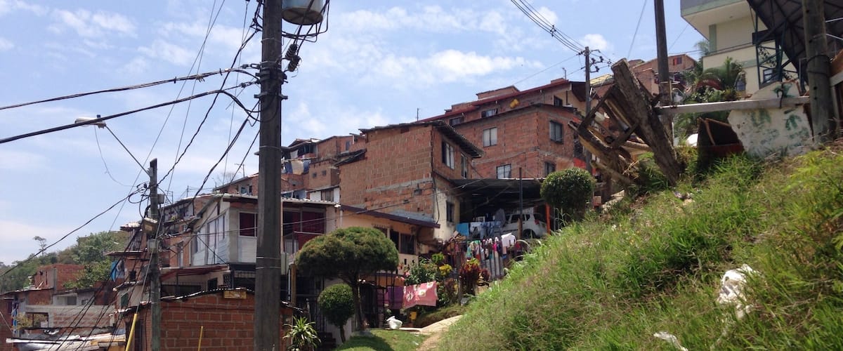 A hillside with a dirt path, buildings, and power lines.