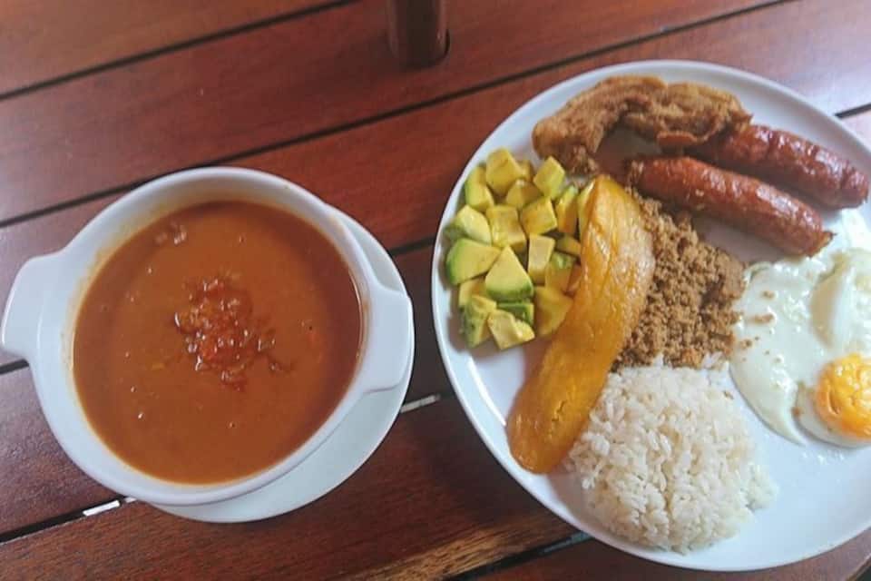 Un plato de comida que incluye arroz, huevos, salchichas y un tazón de sopa.