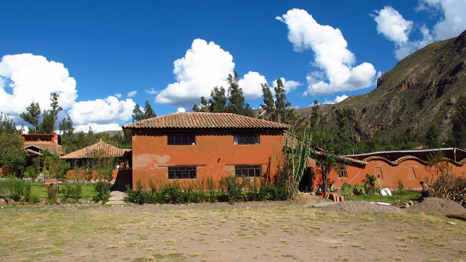 A rural village with terracotta-roofed houses, a clear blue sky, and a mountainous backdrop.