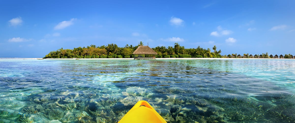 A clear tropical sea with a small island featuring thatched-roof huts and lush greenery.