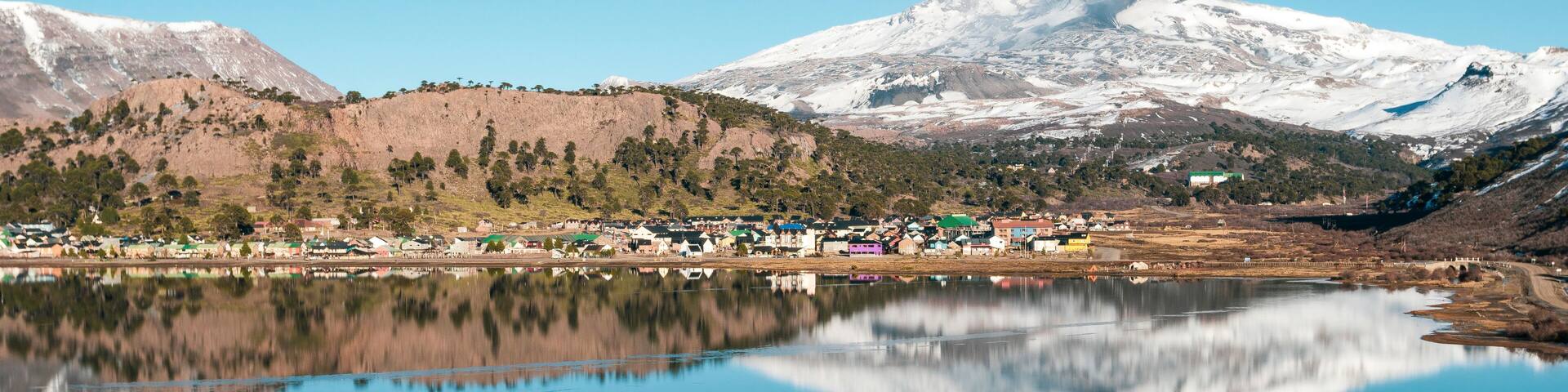 A lake reflecting a town and snow-capped mountains.